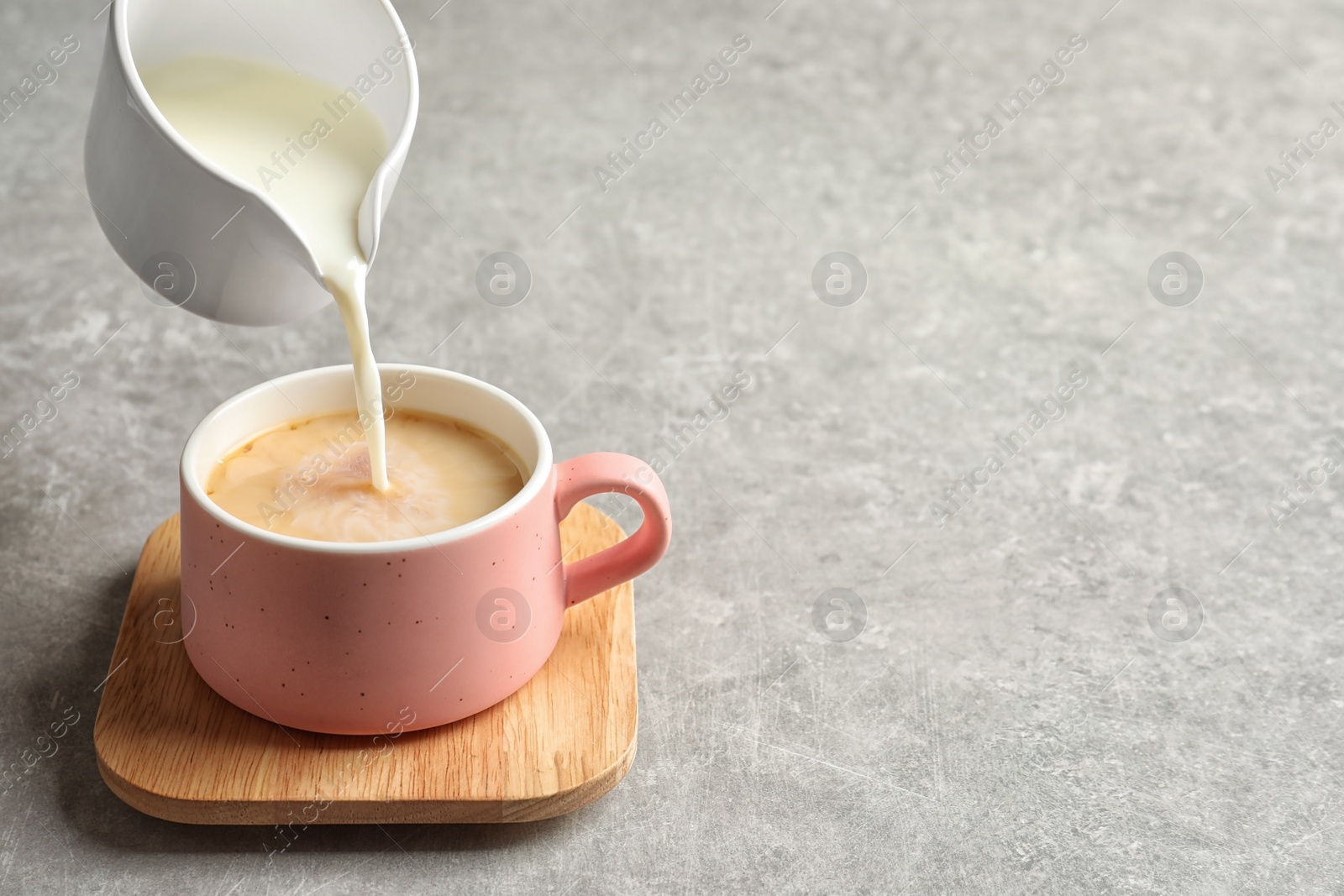 Photo of Pouring milk into cup of black tea on gray table