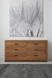 Wooden chest of drawers near white wall in room