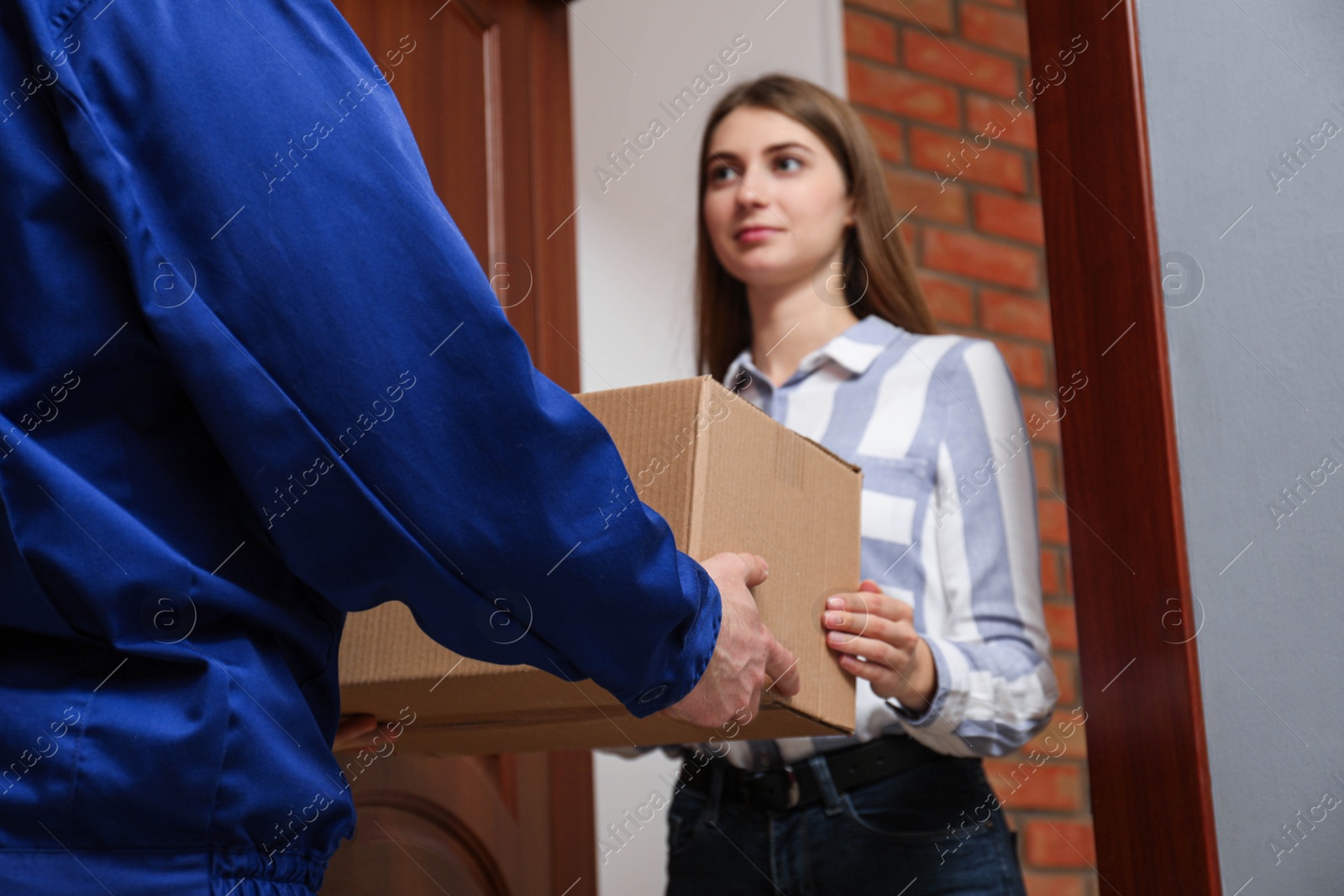 Photo of Young woman receiving parcel from delivery man indoors