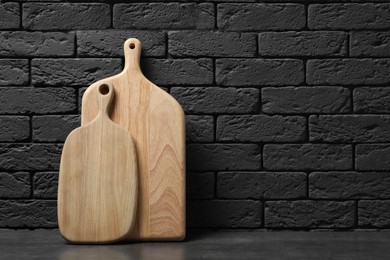 Wooden cutting boards on gray table near dark brick wall, space for text