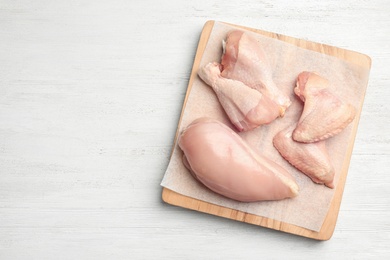 Photo of Cutting board with fresh chicken meat on white wooden table, flat lay. Space for text