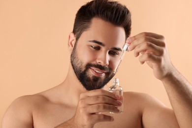 Photo of Handsome man with cosmetic serum in hands on beige background