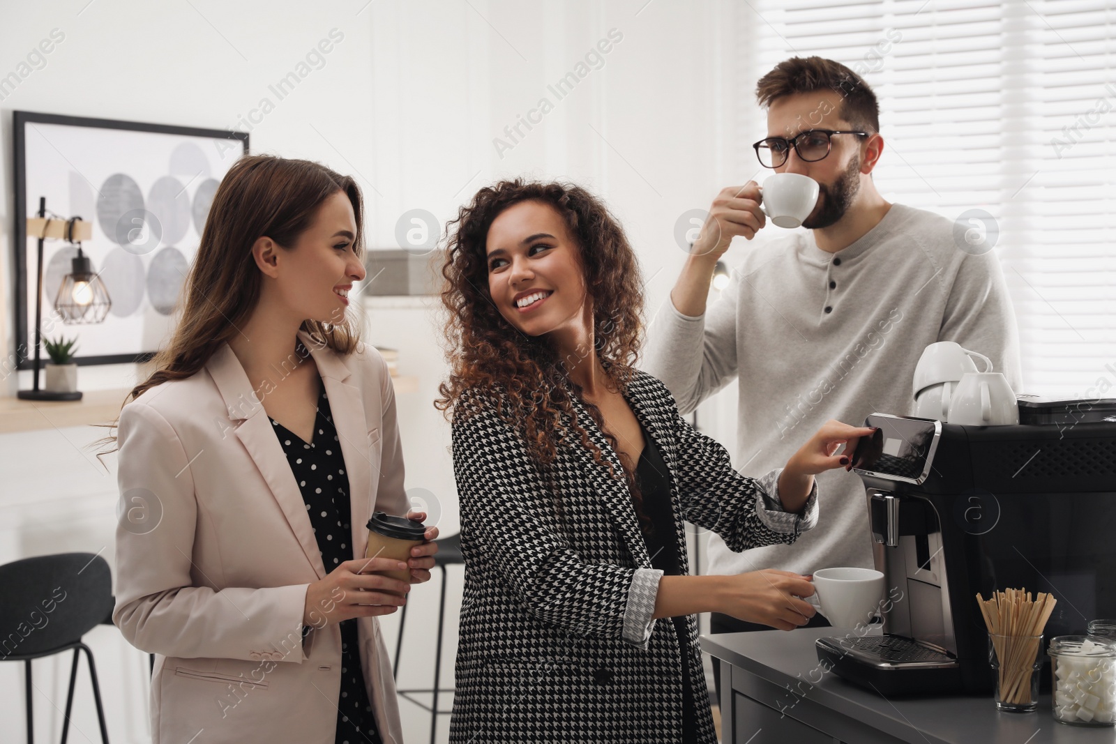 Photo of African American woman talking with colleagues while using modern coffee machine in office
