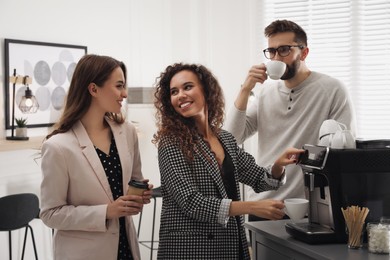 Photo of African American woman talking with colleagues while using modern coffee machine in office