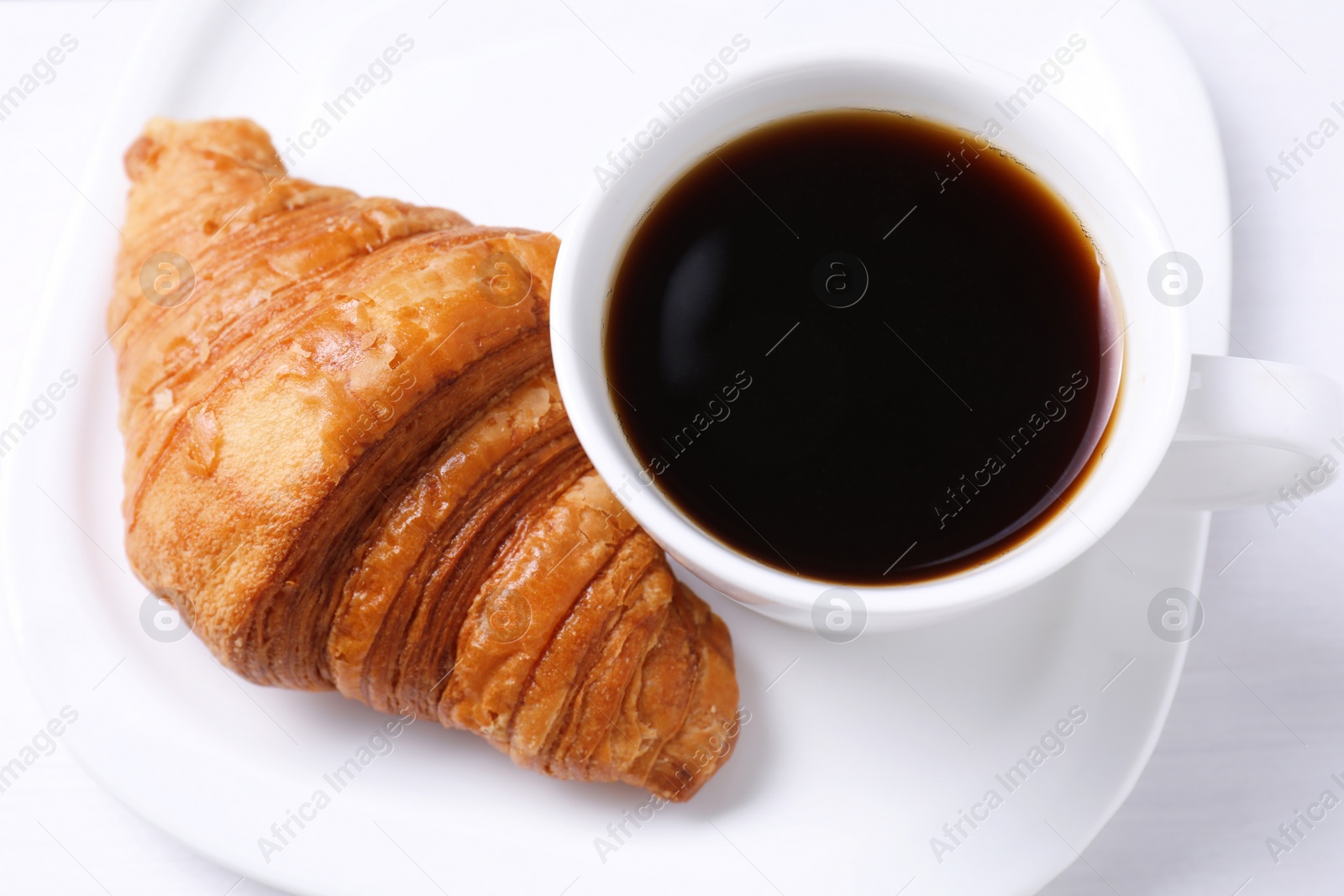 Photo of Tasty breakfast. Cup of coffee and croissant on white wooden table, above view