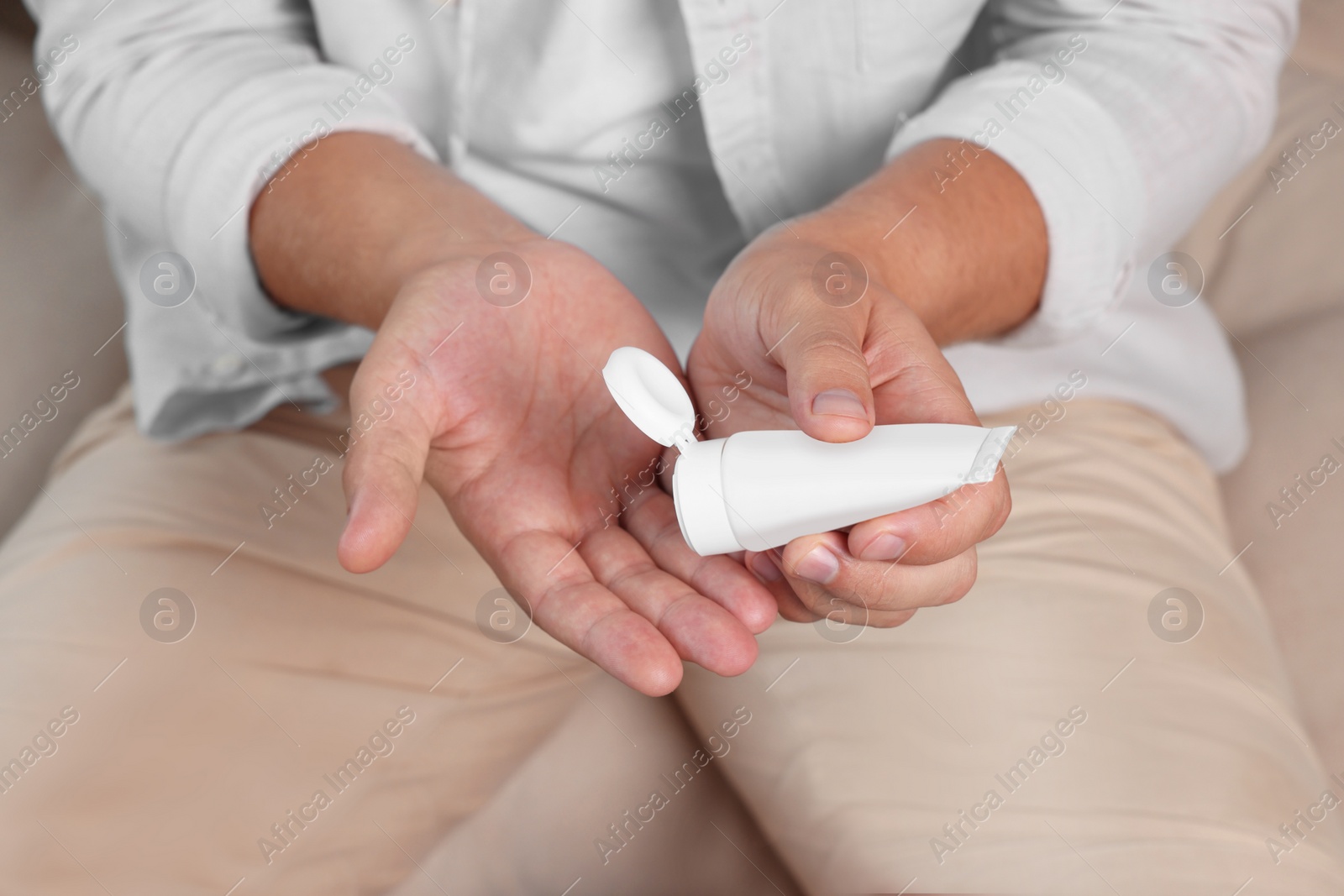 Photo of Man applying hand cream from tube at home, closeup