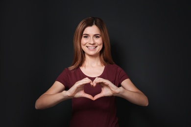 Woman showing HEART gesture in sign language on black background