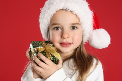 Cute child in Santa hat with Christmas gift on red background