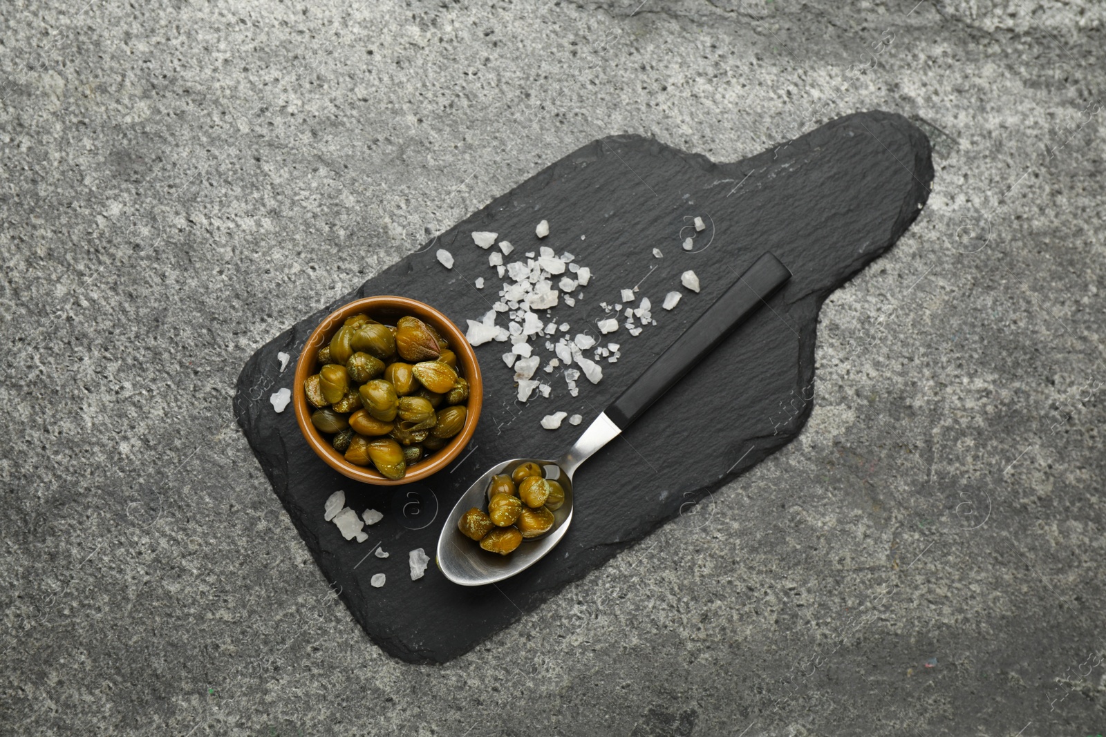 Photo of Tasty capers and salt on grey table, top view