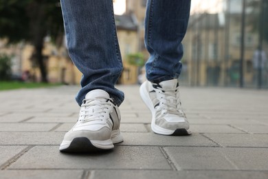 Photo of Man in jeans and sneakers walking on city street, closeup