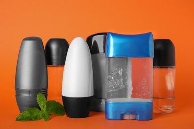 Different natural male deodorants and mint on orange background