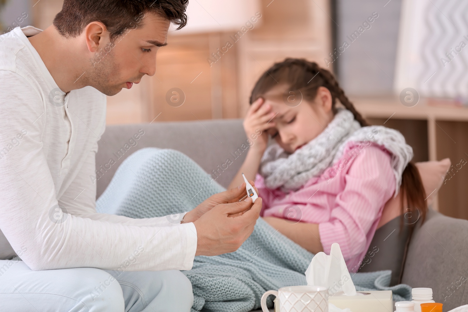 Photo of Father taking care of little daughter suffering from cold on sofa at home