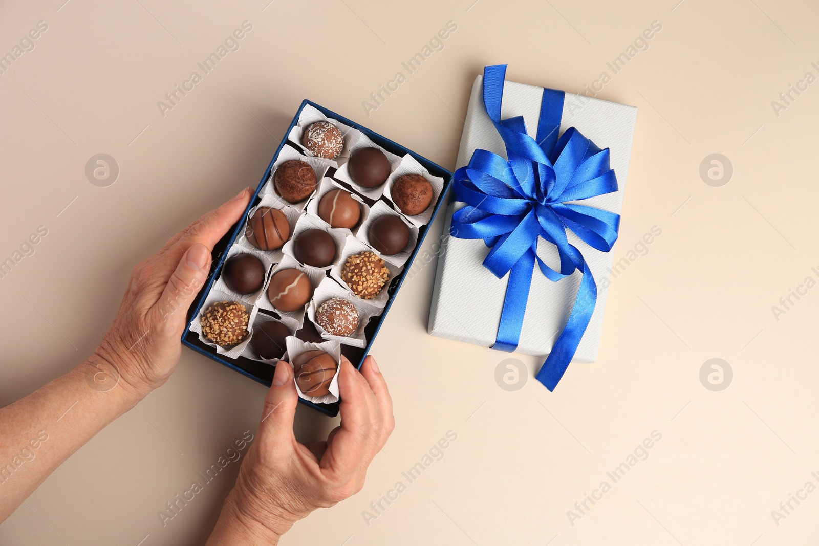 Photo of Woman taking delicious chocolate candy from box on beige background, top view