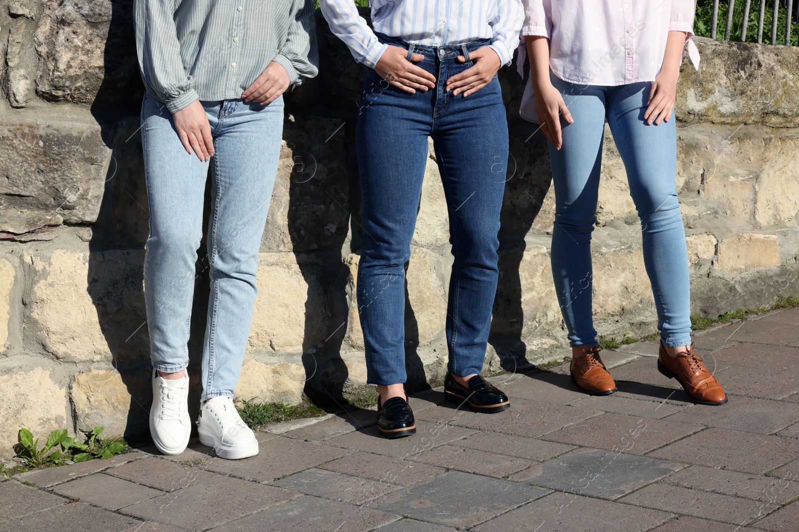 Photo of Women in stylish jeans near stone wall outdoors on sunny day, closeup