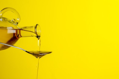 Photo of Pouring cooking oil from jug into spoon on yellow background, closeup. Space for text