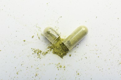 Photo of Broken light green vitamin capsule on white background, top view
