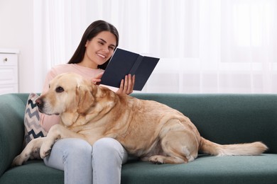Happy woman reading book while sitting with cute Labrador Retriever on sofa at home