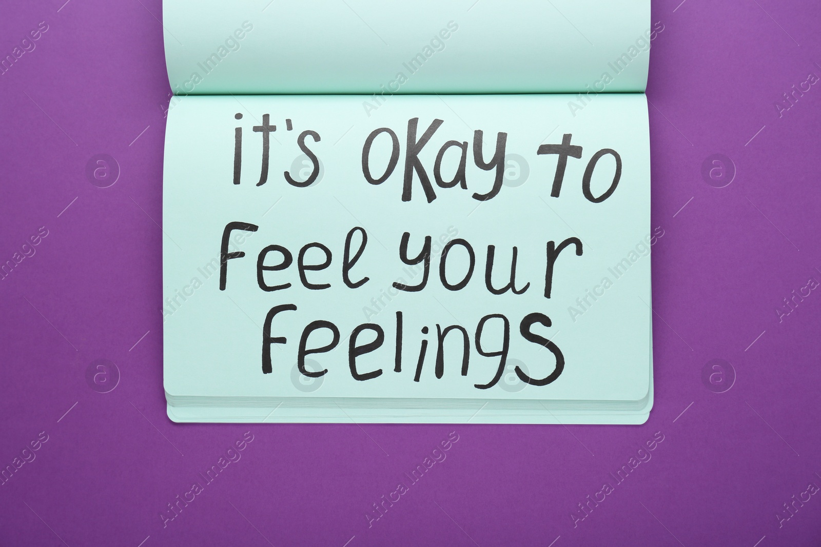 Photo of Notebook with phrase It`s Okay To Feel Your Feelings on purple background, top view