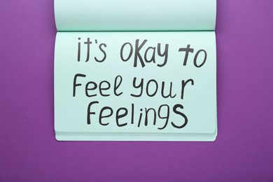 Photo of Notebook with phrase It`s Okay To Feel Your Feelings on purple background, top view