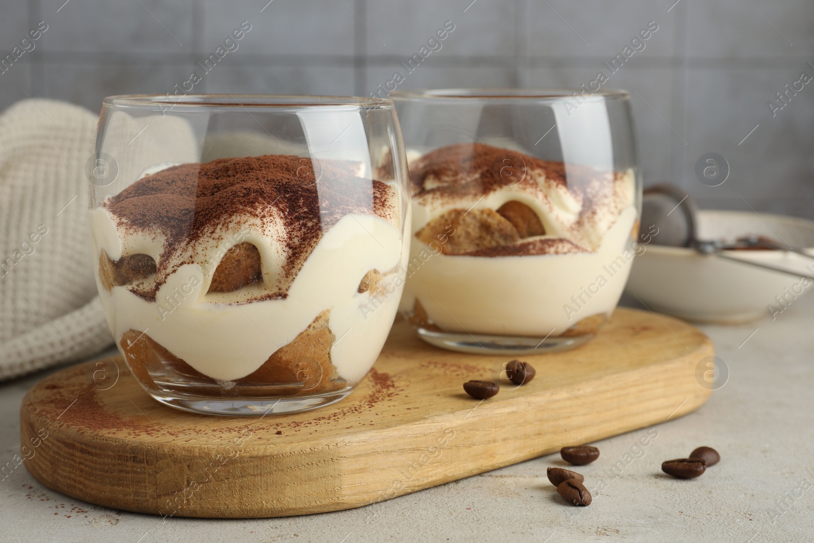 Photo of Delicious tiramisu in glasses and scattered coffee beans on light table