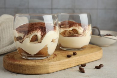 Delicious tiramisu in glasses and scattered coffee beans on light table