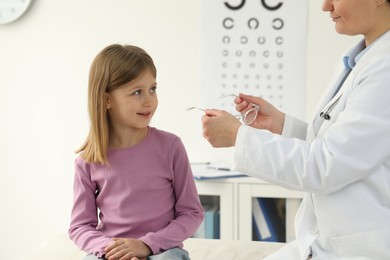 Photo of Vision testing. Ophthalmologist giving glasses to little girl indoors