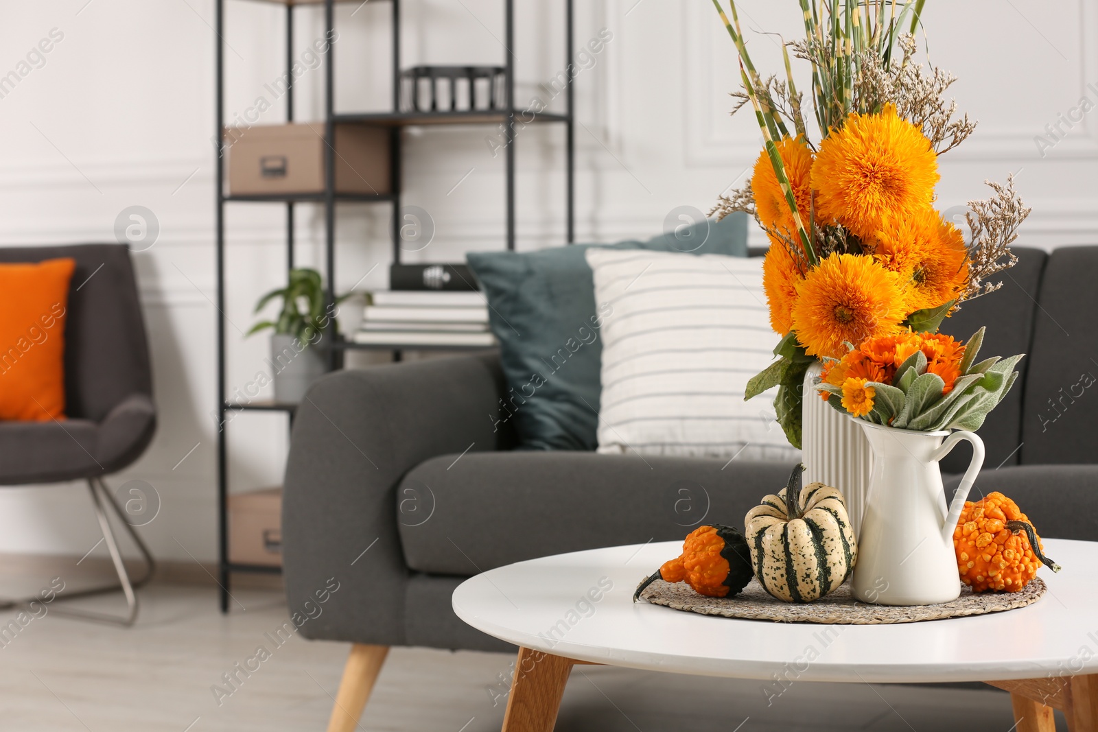 Photo of Beautiful autumn bouquets and pumpkins on coffee table near sofa in room