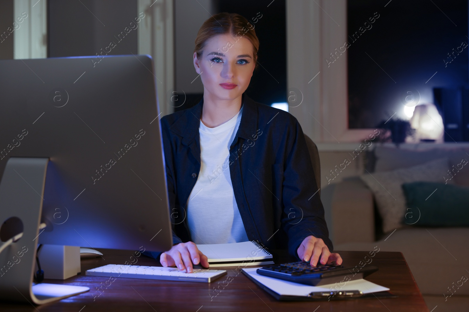 Photo of Home workplace. Woman with calculator near computer at wooden desk in room