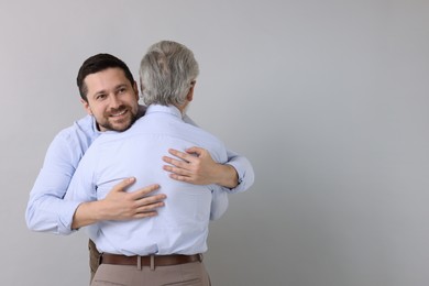 Happy son and his dad hugging on gray background, space for text