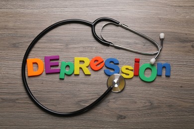 Photo of Word Depression made of colorful letters and stethoscope on wooden table, flat lay