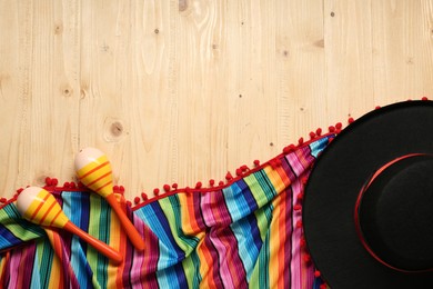 Photo of Mexican sombrero hat, maracas and colorful poncho on wooden background, flat lay. Space for text