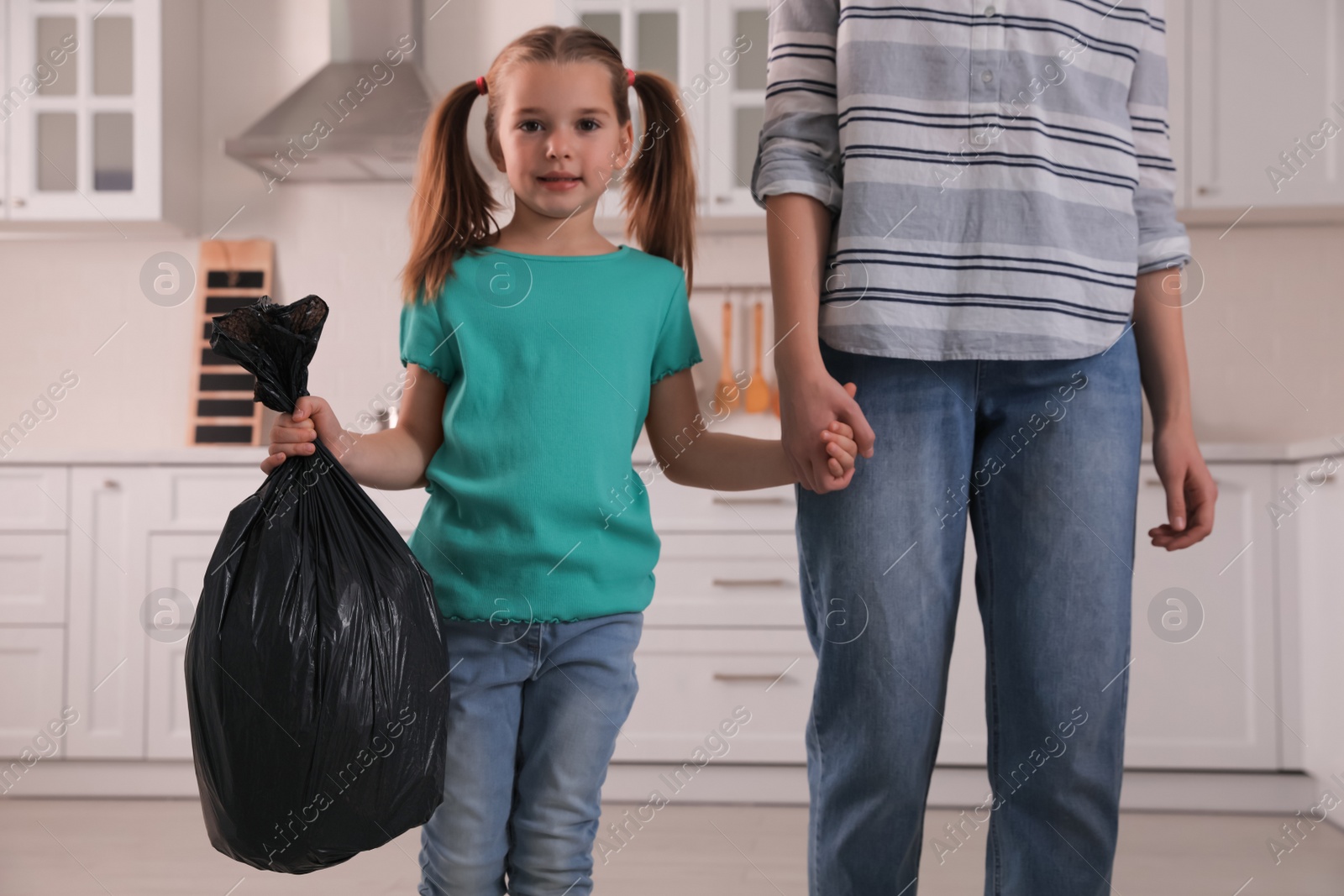 Photo of Little girl holding bin bag full of garbage in kitchen