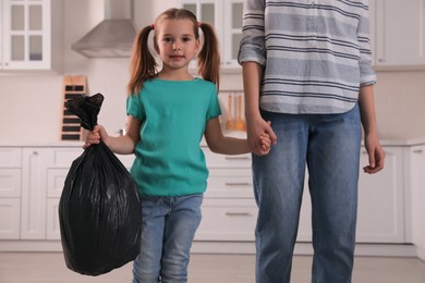 Little girl holding bin bag full of garbage in kitchen