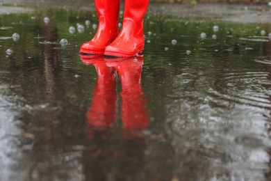 Woman in red rubber boots on rainy day outdoors, closeup