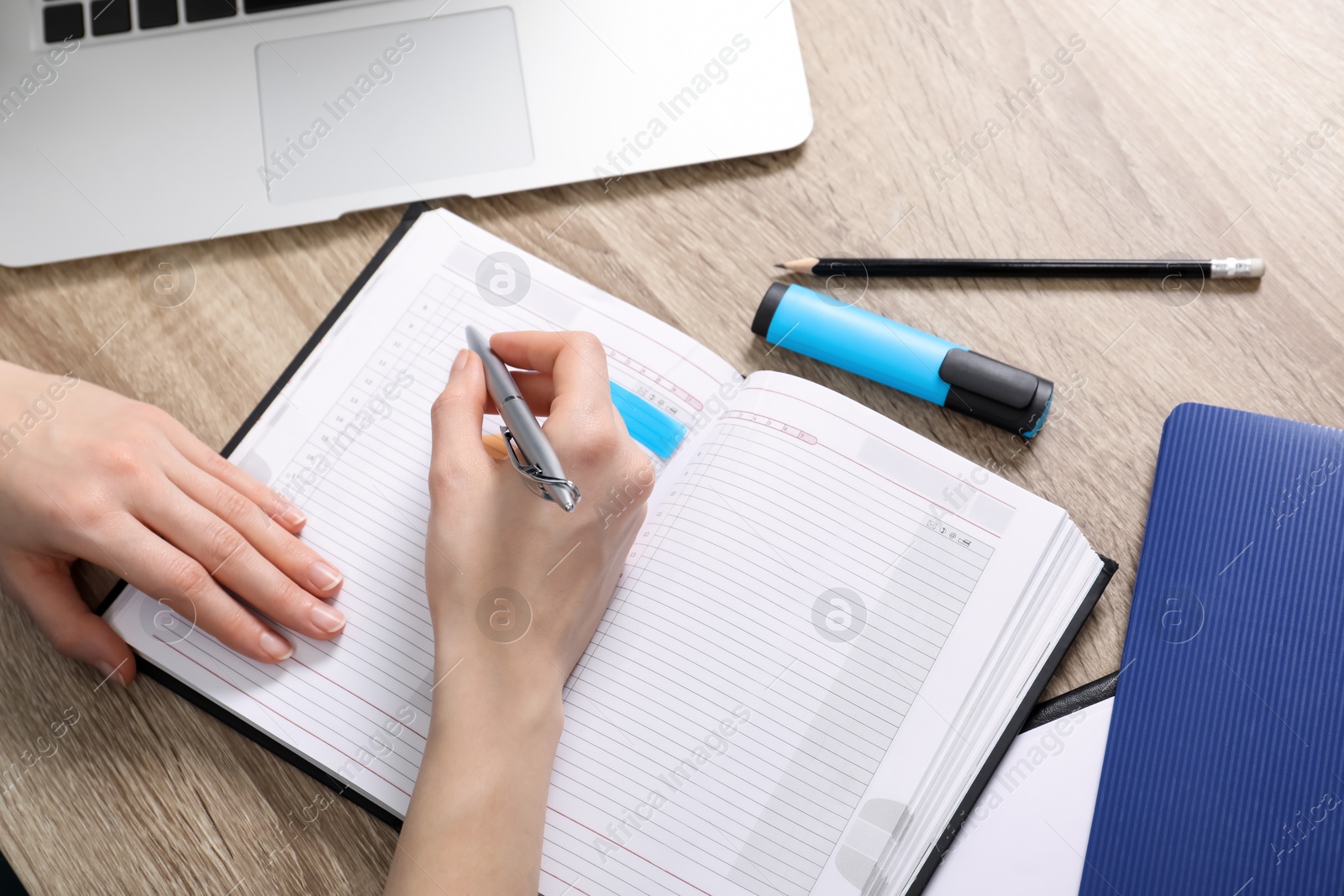 Photo of Woman taking notes at wooden table, closeup