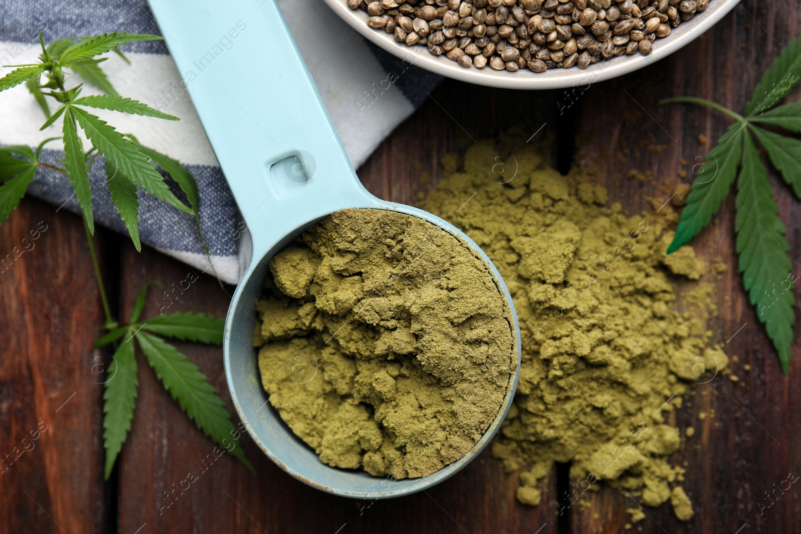 Photo of Hemp protein powder and fresh leaves on wooden table, flat lay