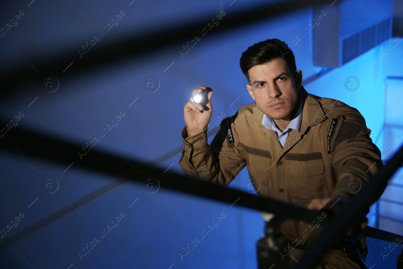 Photo of Professional security guard with flashlight on stairs in dark room