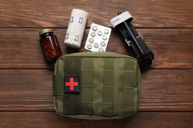 Photo of Military first aid kit, tourniquet, pills and elastic bandage on wooden table, flat lay