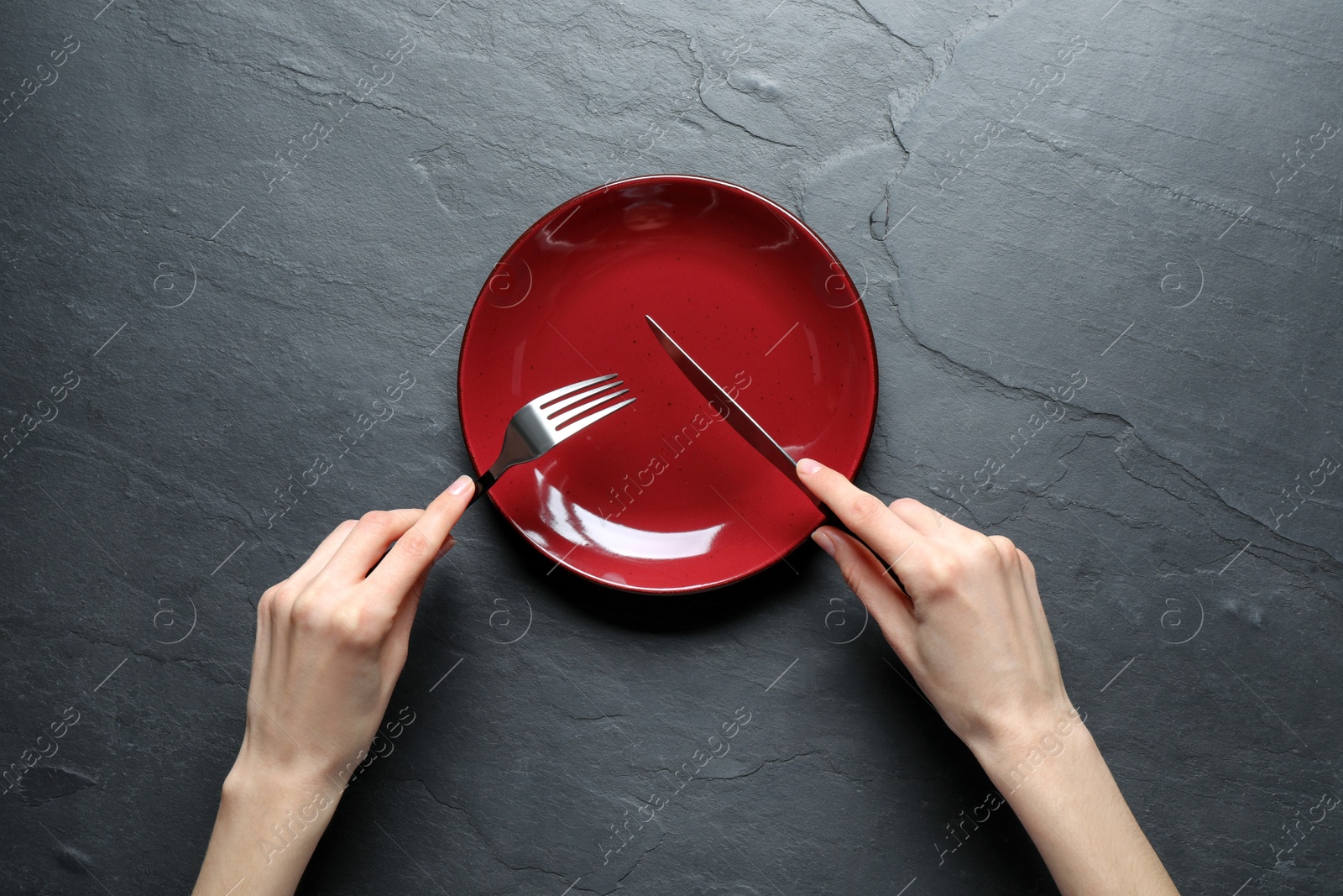 Photo of Woman with fork, knife and empty plate at black table, top view