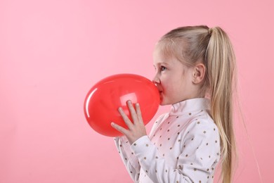 Photo of Cute little girl inflating red balloon on pink background, space for text