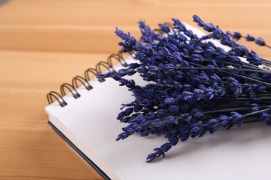 Photo of Bouquet of beautiful preserved lavender flowers and notebook on wooden table, closeup. Space for text