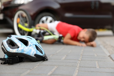 Photo of Little boy fallen from bicycle after car accident outdoors, focus on helmet