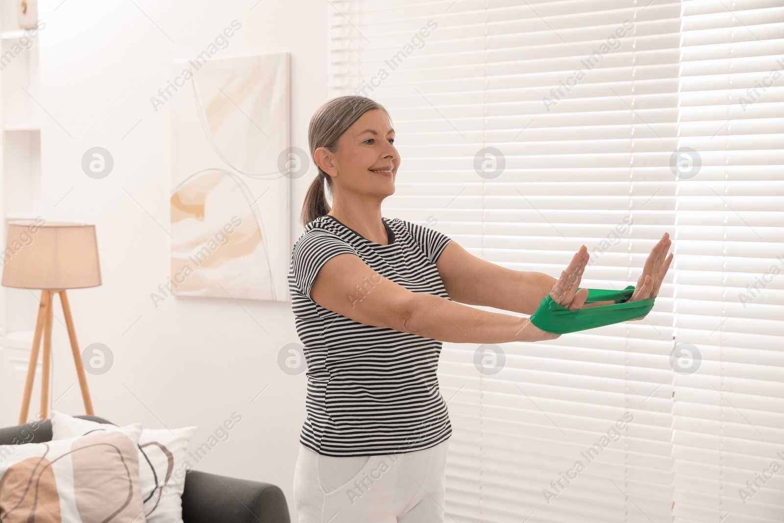 Photo of Senior woman doing exercise with fitness elastic band at home