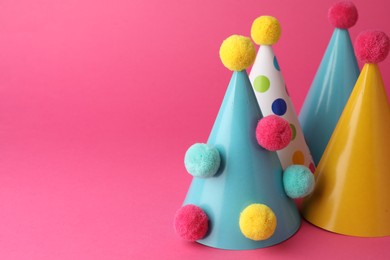 Beautiful party hats with pompoms on pink background, space for text