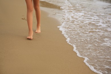 Photo of Little girl walking on sandy beach near sea, closeup. Space for text