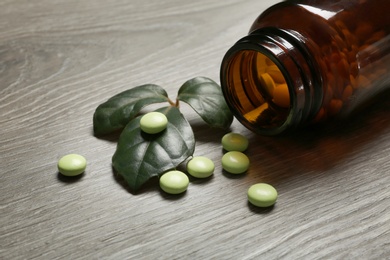 Photo of Bottle with vitamin pills and green leaves on table, closeup