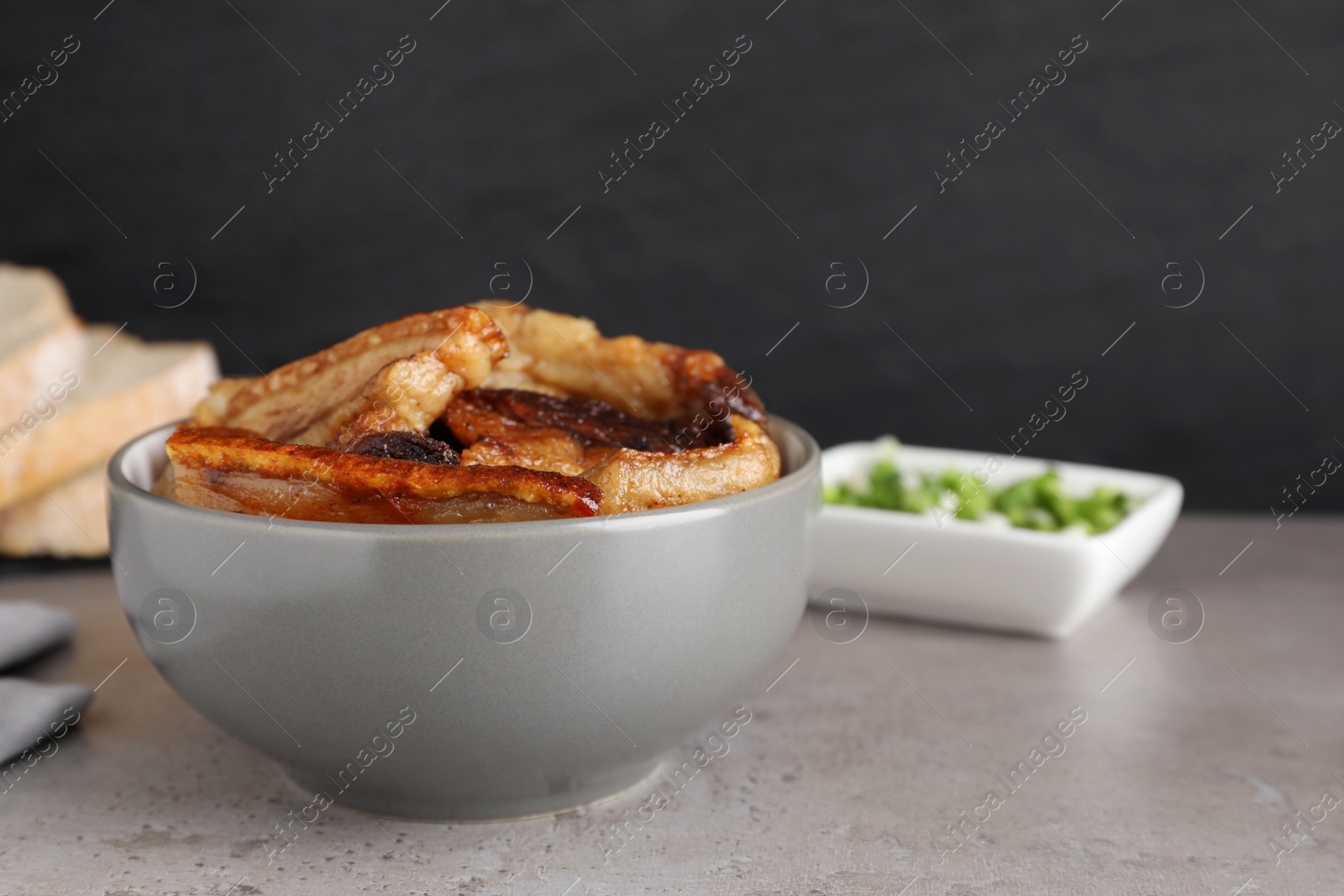 Photo of Bowl with tasty fried pork fatback slices on grey table, space for text