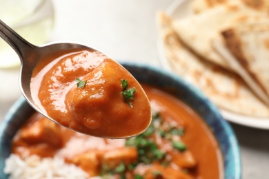 Spoon with tasty butter chicken over bowl of meal, closeup