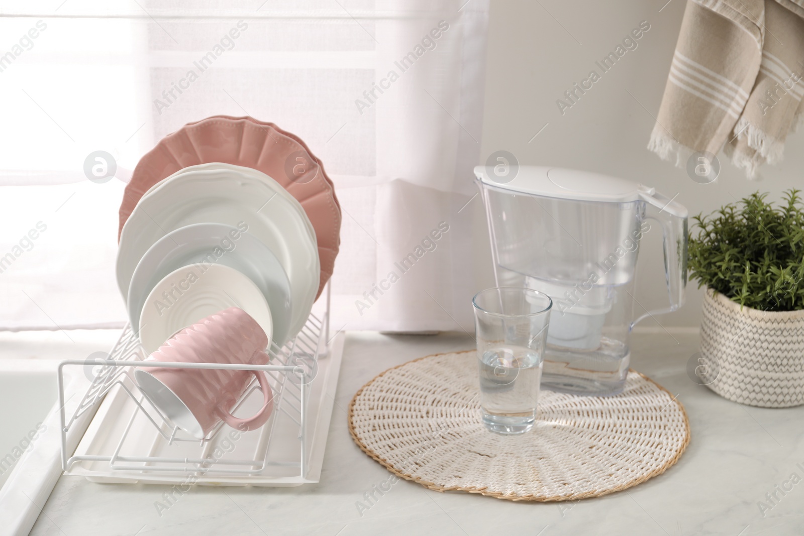 Photo of Drainer with different clean dishware, glass and cup on light table indoors