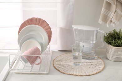 Photo of Drainer with different clean dishware, glass and cup on light table indoors